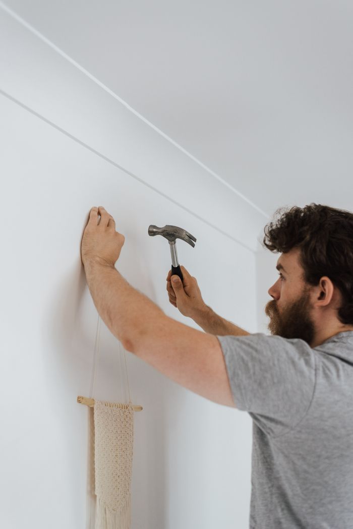 Side view of bearded craftsman with hammer putting decoration on wall during renovation works